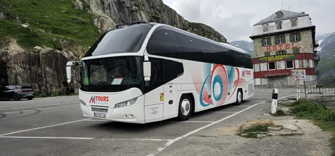 Touring coach on a mountain road beside a stone building